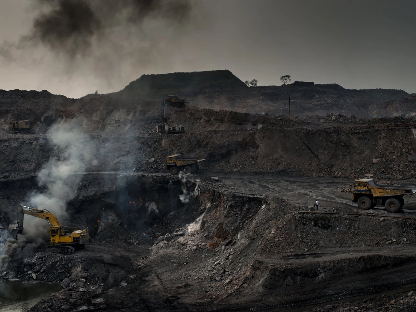 An open-cast coal mine: haul trucks and an excavator working a smoking pit